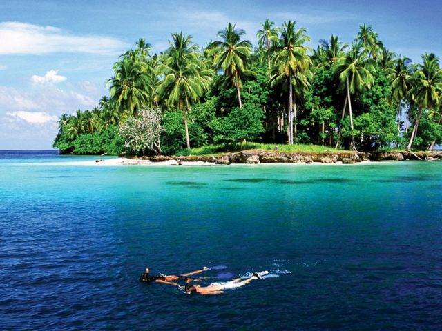 Two people snorkel near a tropical island.