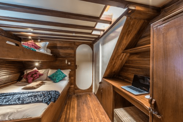 A cabin on a boat with bunk beds and a desk.