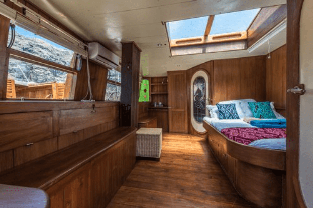A cabin on a boat with wooden walls and a bed.