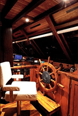 The interior of a wooden boat with a steering wheel.