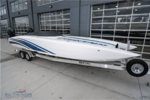 A white speed boat, the 2018 Fountain 32 Thundercat, on a trailer in front of a building.
