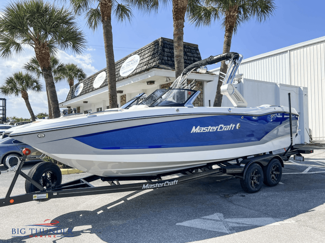 A blue and white boat, a 2023 master craft x24, parked in a parking lot.