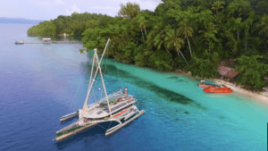 From a lofty vantage point, behold a majestic boat anchored at the idyllic harbor of a tropical island.