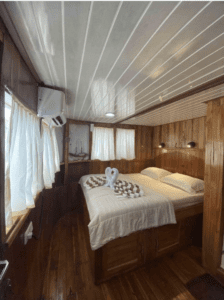 A room on a boat with wooden floors and a bed, converted into the luxurious setting of 2024 KLM SINAR PAGI.